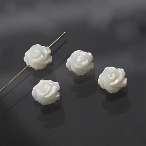 Macro detail of white carved mother-of-pearl rose beads showing the pre-drilled DIY holes