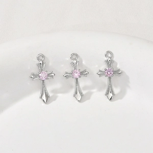Macro detail of silver cross pendant with pink zircon and intricate embossed texture
