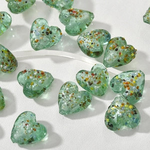 Dettaglio macro di perline di vetro verde a forma di cuore con macchie colorate per gioielli