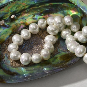 Iridescent white pearl necklace displayed in a colorful abalone shell background