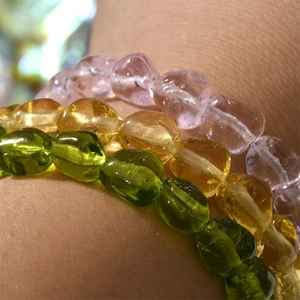 Close-up of three colorful baroque glass bead bracelets in green, amber, and pink tones