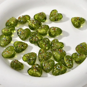 Dettaglio macro di perline di vetro verde a cuore con macchie colorate in vassoio