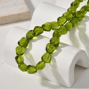 Olive green irregular baroque glass beads on a white minimalist stone display arch