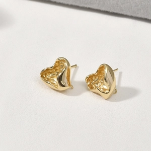 Macro view of 14k gold-plated heart studs featuring irregular textured lava surface