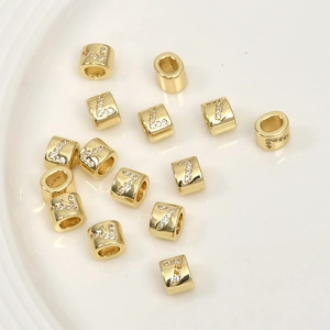 Macro shot of gold cylinder beads with letter L and 7 zircon inlay for jewelry making