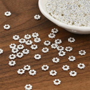 Bulk silver flower spacer beads for DIY jewelry making displayed on a wooden surface