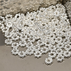 Pile of silver snowflake spacer beads with central holes for DIY jewelry making crafts
