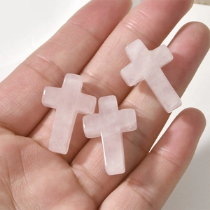 Three pink quartz crystal cross pendants for jewelry making held in hand for scale