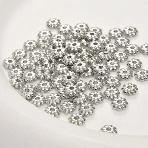 Macro shot of silver sunflower spacer beads for DIY jewelry making piled on a white tray