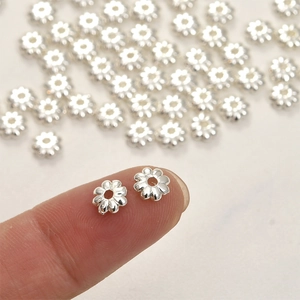 Macro detail of silver sunflower spacer beads for DIY jewelry making on fingertips