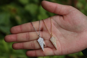Macro detail of gold and silver hip-hop arrow pendants with micro-pave cubic zirconia