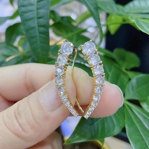 Orecchini a semicerchio placcati in oro con cristalli scintillanti tenuti in mano
