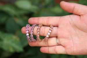 Vista detallada de aretes de aro en C con circonitas de corazón rosa sostenidos a mano