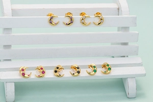 Set of five gold crescent moon stud earrings with colorful zircon stones on display