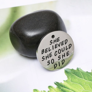 Makroaufnahme von rundem Edelstahl-Anhänger mit She Believed She Could Gravur in Silber