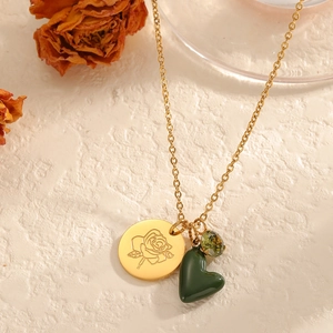 Goldene Kette mit gravierter Rose und dunkelgrünem Herzanhänger auf Stein