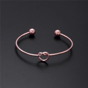 Eleganter rosévergoldeter Knotenarmreif mit polierten Metallperlen auf dunklem Grund