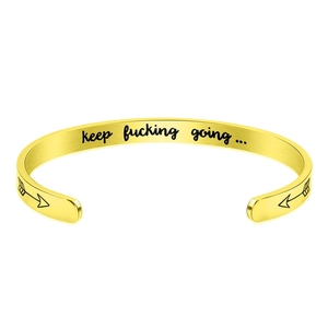 Macro shot of gold cuff bracelet with 'keep fucking going' engraving and arrow detail