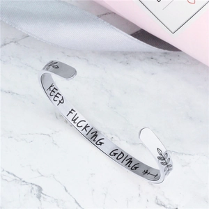 Polished stainless steel cuff bracelet with Keep Fucking Going engraving on marble surface