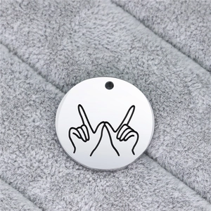 Macro shot of silver stainless steel round pendant with laser-engraved hand gesture design