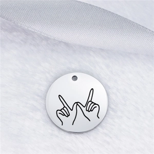 Macro shot of silver round stainless steel pendant with hand gesture line engraving