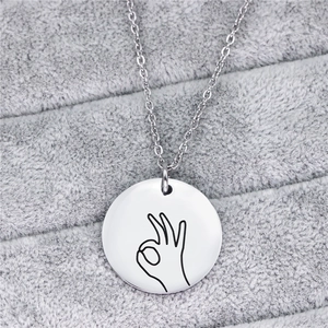 Dettaglio macro della collana in acciaio argento con pendente circolare gesto OK