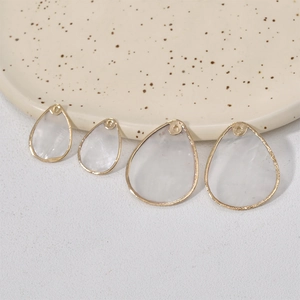 Détail de pendentifs gouttes en nacre avec bordure dorée sur un plateau pour bijoux DIY