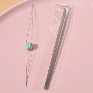 Macro shot of flexible beading needle threading a blue pumpkin bead on pink tray