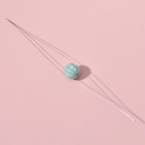 Extra fine beading needle threading a light blue pumpkin ceramic bead on pink background
