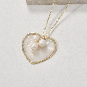 Détail d'un pendentif cœur en nacre avec bord doré, perles et fine chaîne dorée