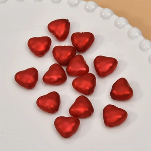 Detail view of fourteen red matte heart-shaped beads on a white relief porcelain plate