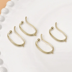 Close-up of four 14k gold-plated U-shaped ear clip findings on a white ceramic plate