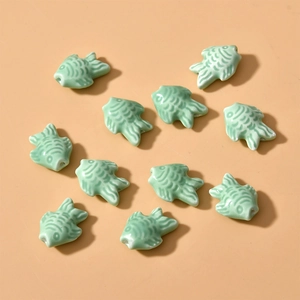 Flat lay macro of eleven light green fish-shaped ceramic beads for DIY jewelry making