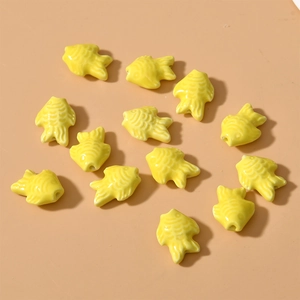 Macro detail of yellow fish-shaped ceramic beads with glossy glaze for jewelry making