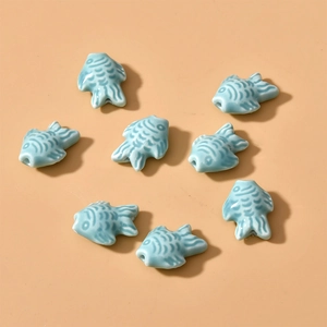 Close-up of light blue ceramic fish beads for DIY jewelry making with glazed scale texture
