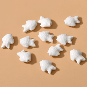 Macro shot of white ceramic fish beads with glossy glaze and detailed scale textures