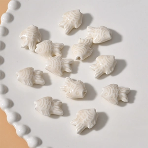 Close-up of 12 cream white ceramic fish beads with glazed texture for DIY jewelry making