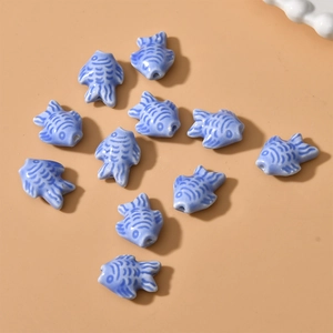 Flat lay of light blue ceramic fish beads with hand-painted scales for DIY jewelry making
