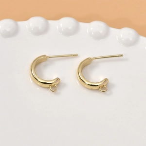 Close-up of 14k gold-plated C-shaped stud earrings on a white ceramic tray