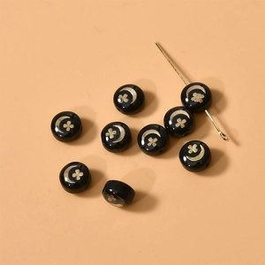 Detalle de cuentas redondas negras y doradas con lunas y tréboles para joyería artesanal