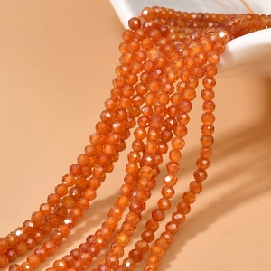 Macro detail of 2mm orange faceted zircon beads spilling from a ceramic bowl for DIY jewelry