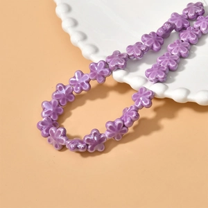 Detailed view of lavender ceramic flower beads for DIY jewelry making on white scalloped plate