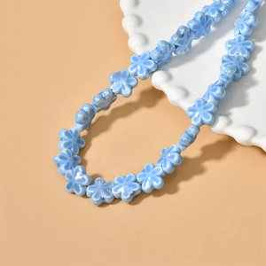 Close-up of light blue ceramic flower beads on a white tray for DIY jewelry making