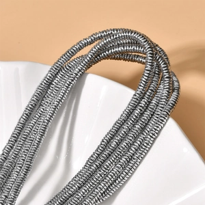 Macro shot of silver wave disc hematite beads on a white textured ceramic tray