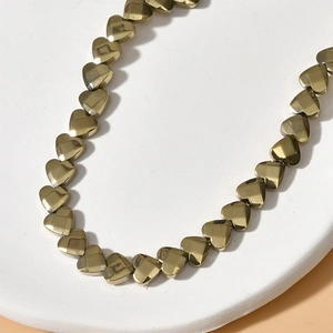 Macro shot of 6mm vintage gold heart-shaped metal beads arranged on a white tray