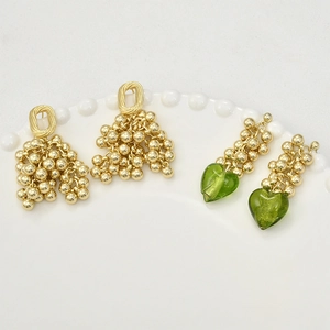 Elegant gold beaded grape clusters and green resin heart earrings on white tray