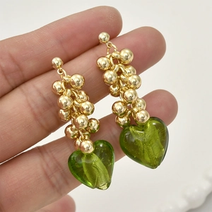 Detail of long drop earrings featuring gold beaded spheres and a green heart pendant