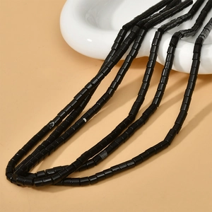 Gros plan de perles cylindriques en pierre naturelle noire 4x4mm sur plateau blanc