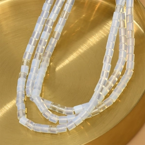 Détail macro de perles en cristal cylindriques blanc laiteux de 4 mm sur plateau doré