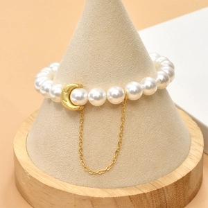 Close-up of pearl bracelet with golden moon pendant on a minimalist display stand